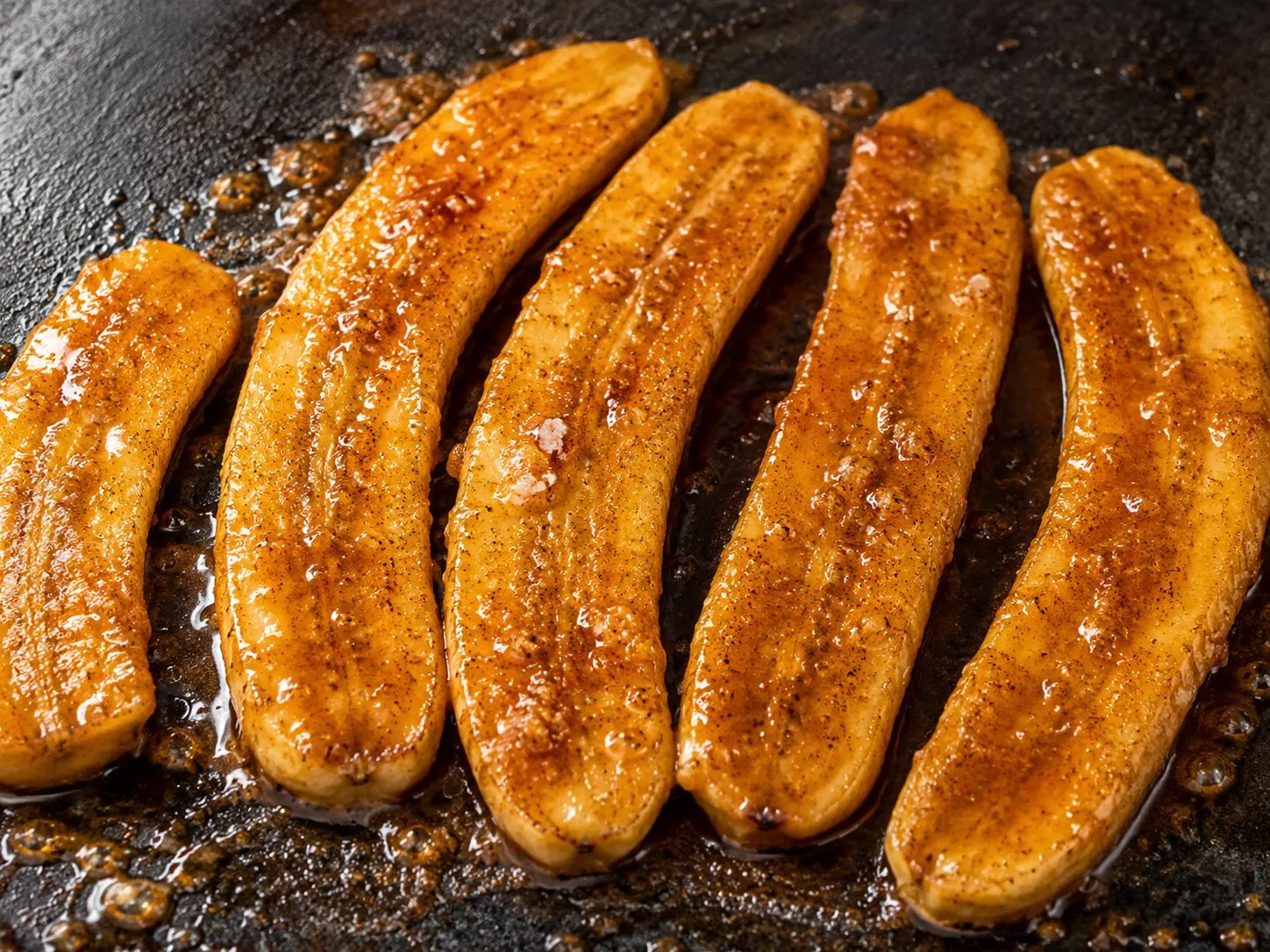 Banana halves caramelizing in brown sugar rum sauce on a Blackstone griddle