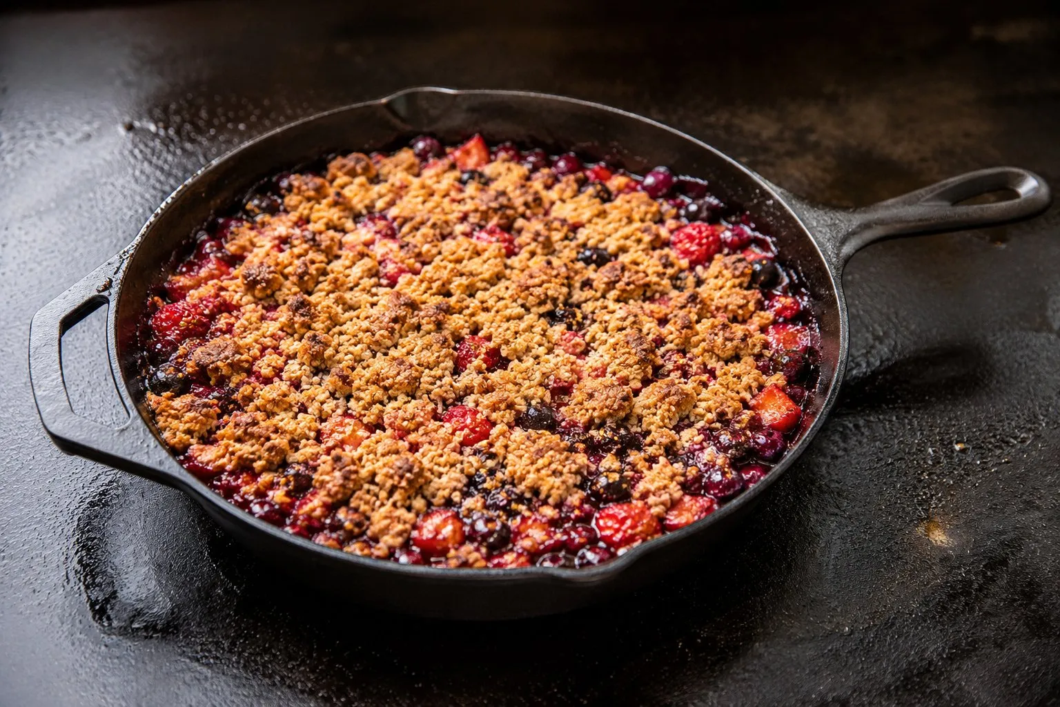 Berry crisp with golden oat crumble bubbling in a cast iron skillet on a Blackstone griddle