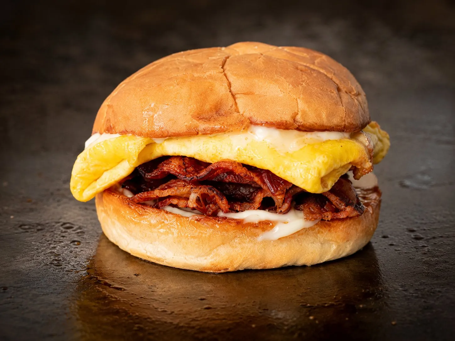 Breakfast sandwich with folded egg, crispy bacon, and melted cheese on a toasted brioche bun
