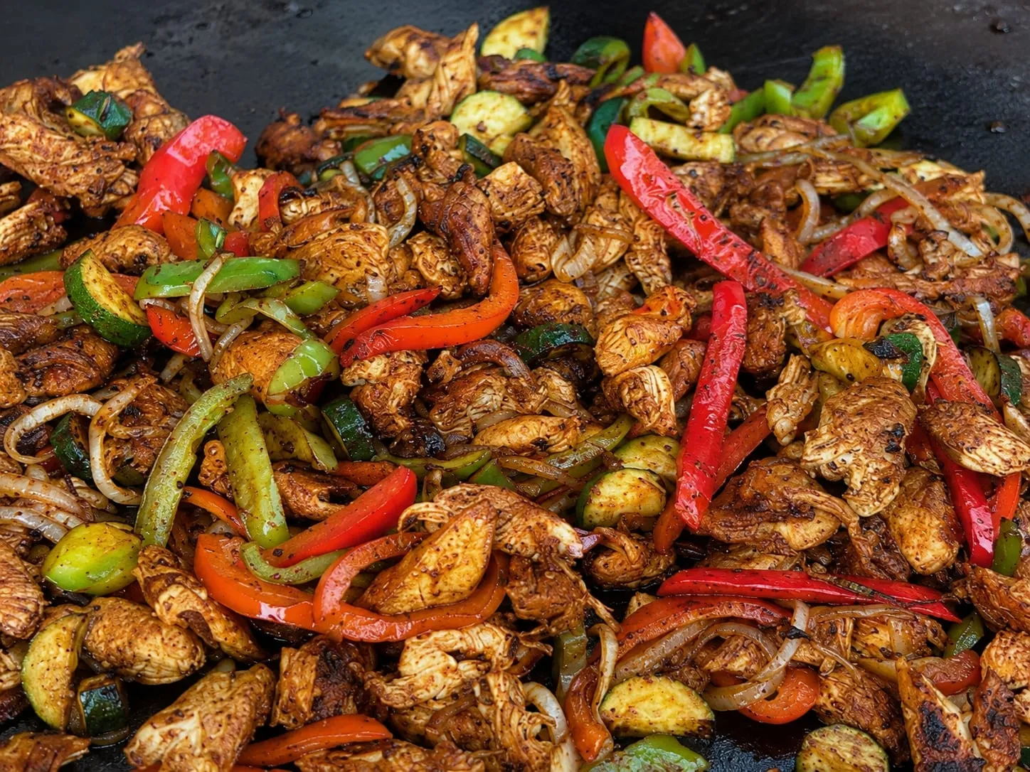 Blackstone chicken fajitas with charred peppers and onions on a flat-top griddle