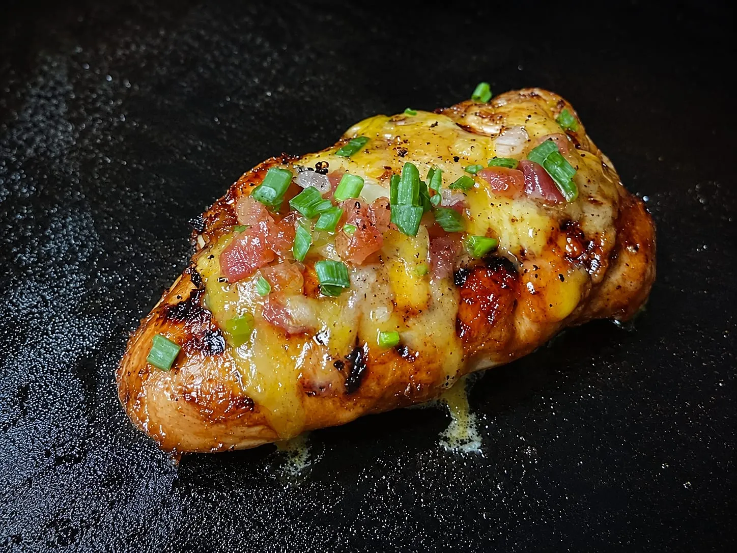 Loaded grilled chicken breast on a Blackstone griddle with melted cheese, tomatoes, and green onions