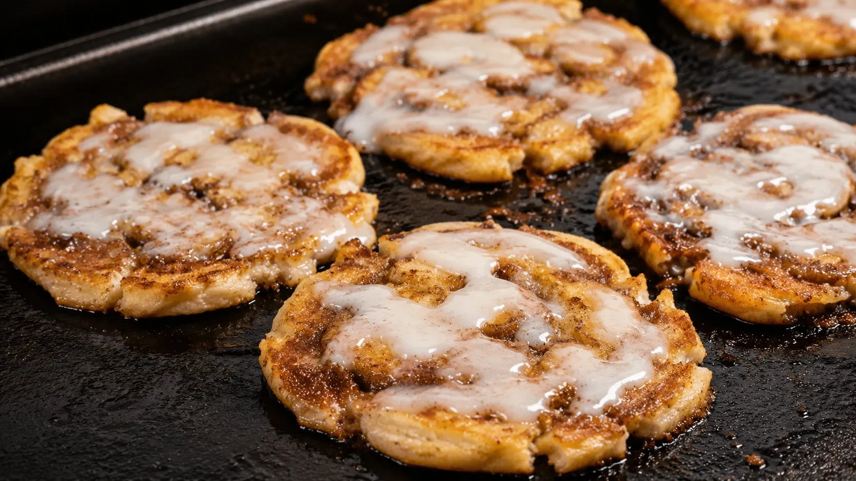 Smashed cinnamon rolls with melted icing cooking on a Blackstone griddle