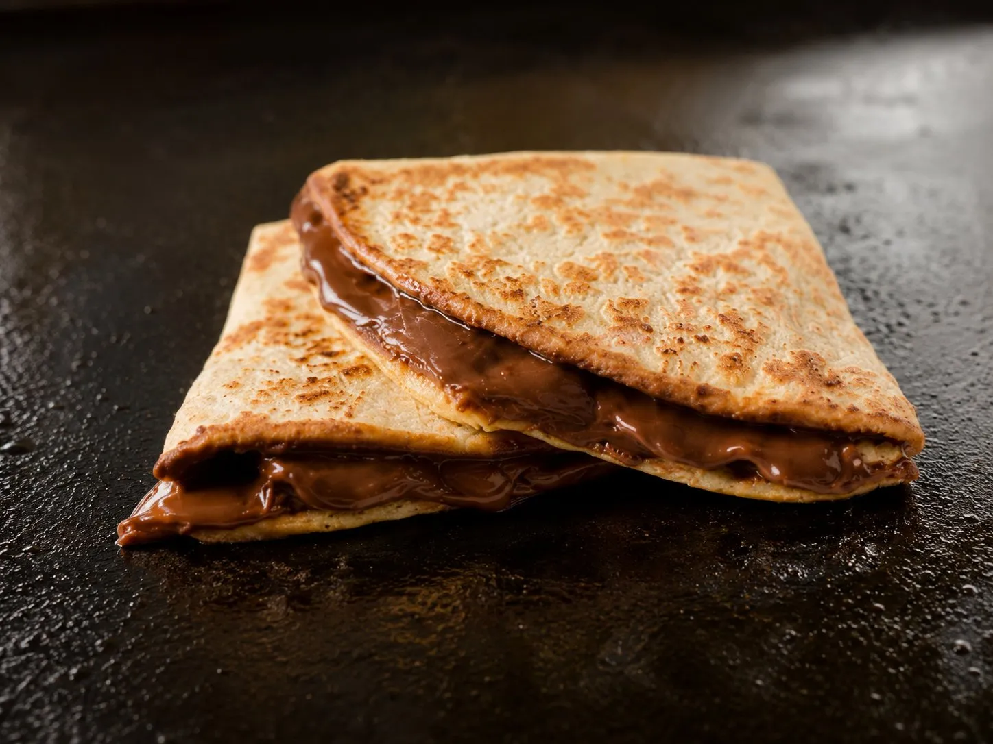 Folded chocolate dessert quesadilla with melted filling oozing out on a Blackstone griddle