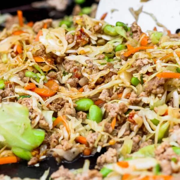 Egg roll in a bowl on a Blackstone griddle with ground pork, cabbage, and carrots in a ginger-soy sauce