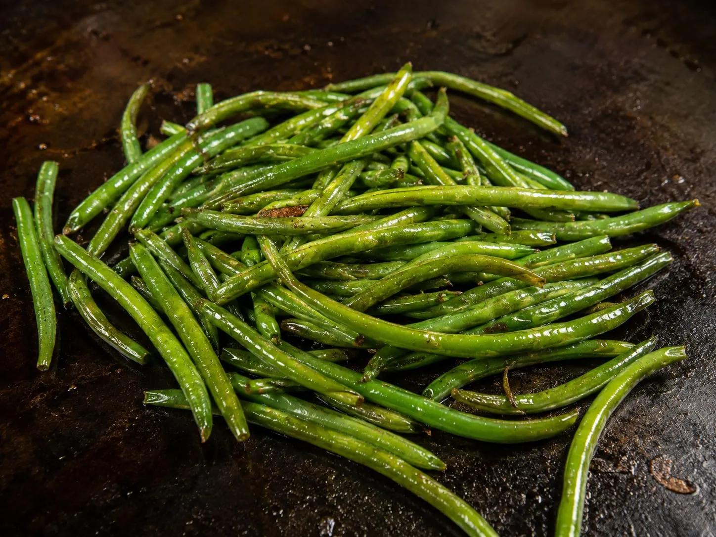 Blistered green beans glistening on a seasoned Blackstone griddle surface