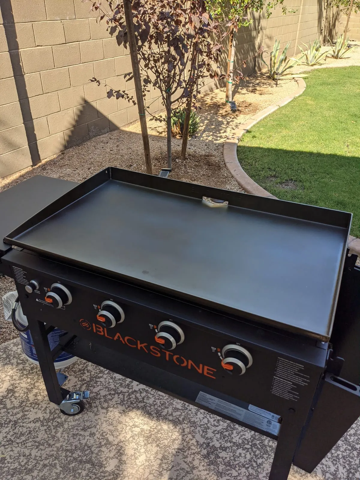 A well-seasoned 4-burner Blackstone 36-inch griddle set up on a backyard paver patio
