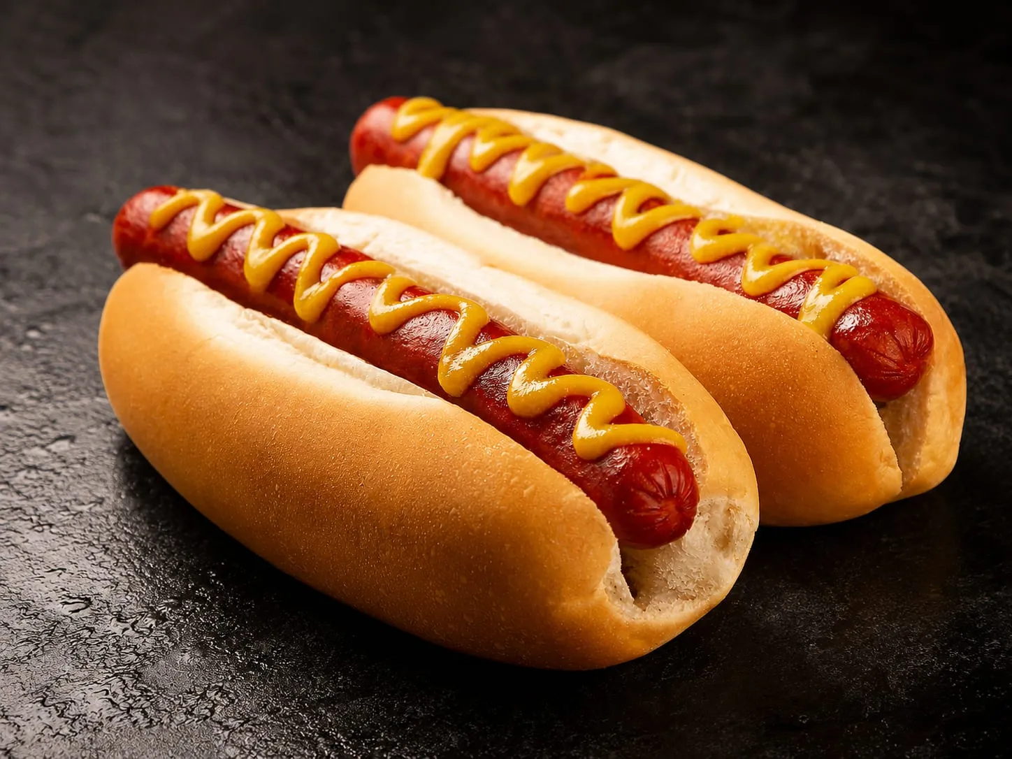 Charred hot dogs searing on a Blackstone griddle with toasted buns