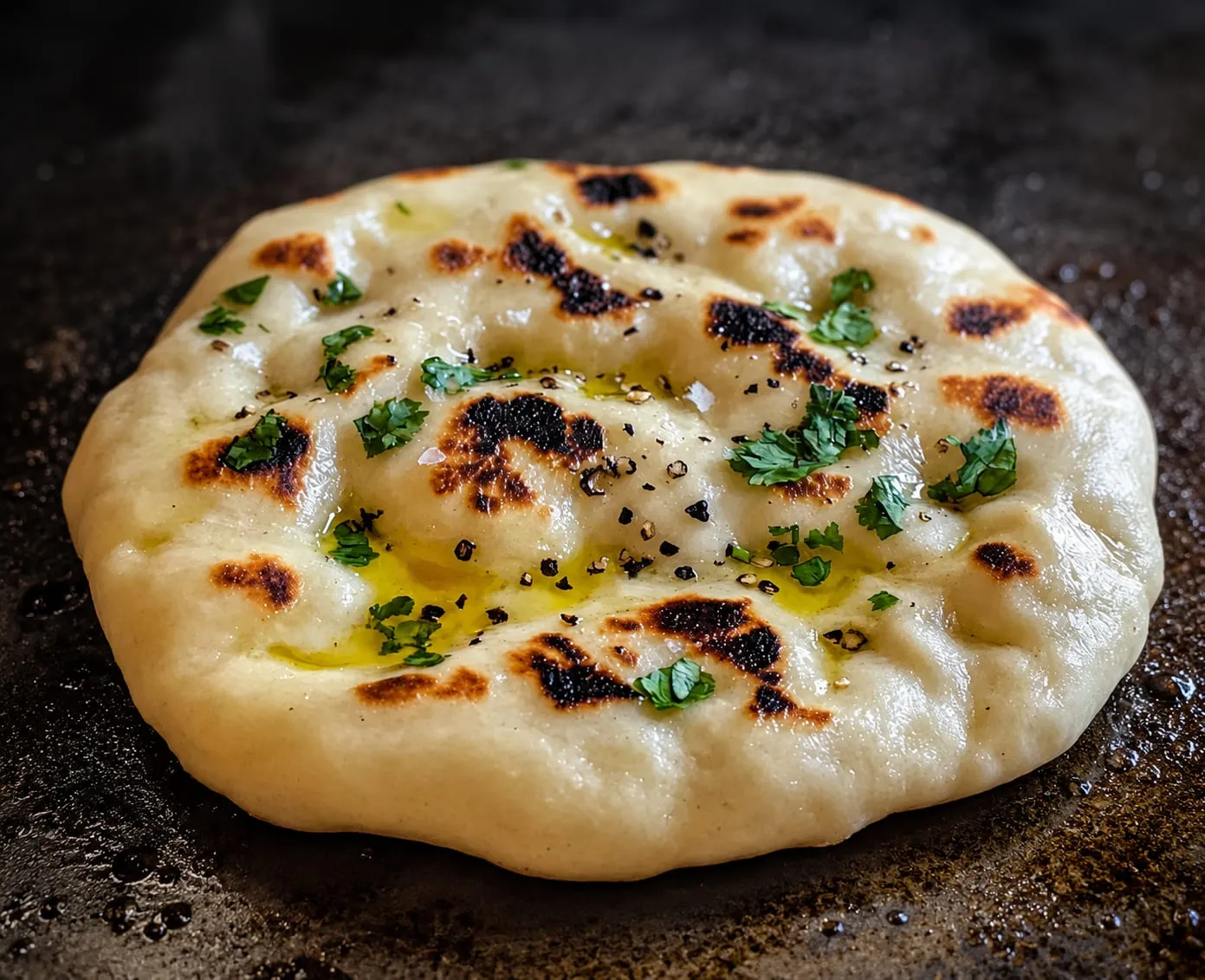 Charred naan bread with golden spots cooking on a Blackstone griddle