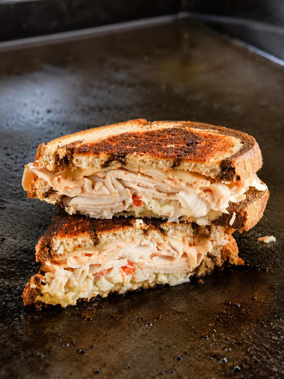 Rachel sandwich on a Blackstone griddle with turkey, Swiss, and coleslaw on toasted rye