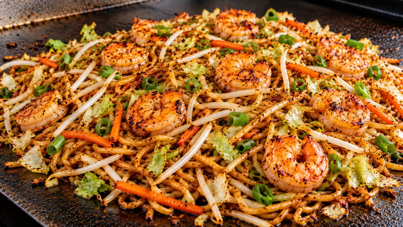 Shrimp chow mein with seared shrimp, crisped noodles, cabbage, carrots, bean sprouts, and green onions on a Blackstone griddle