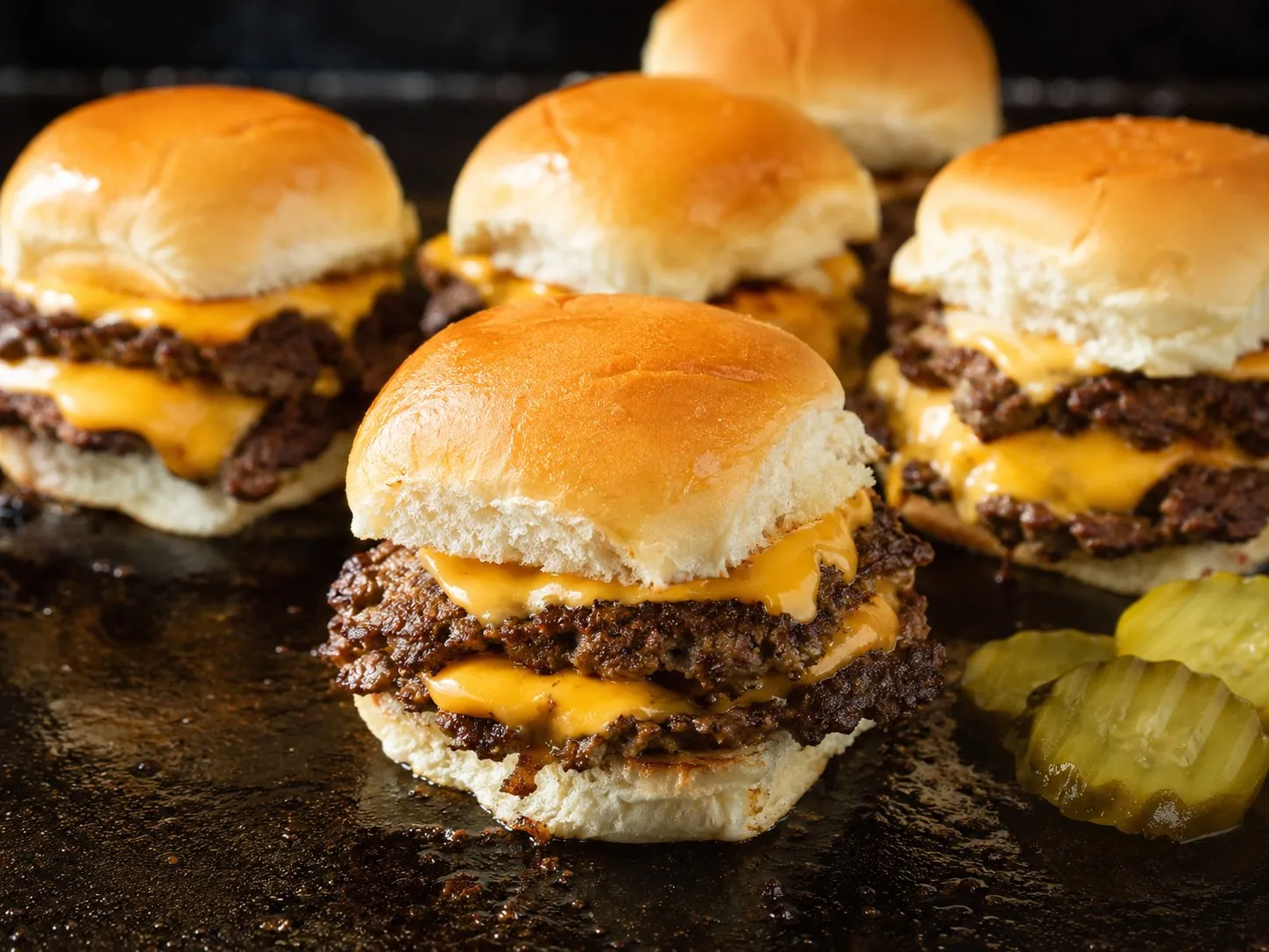 Double-stacked smash sliders with melted cheese on Hawaiian rolls on a Blackstone griddle